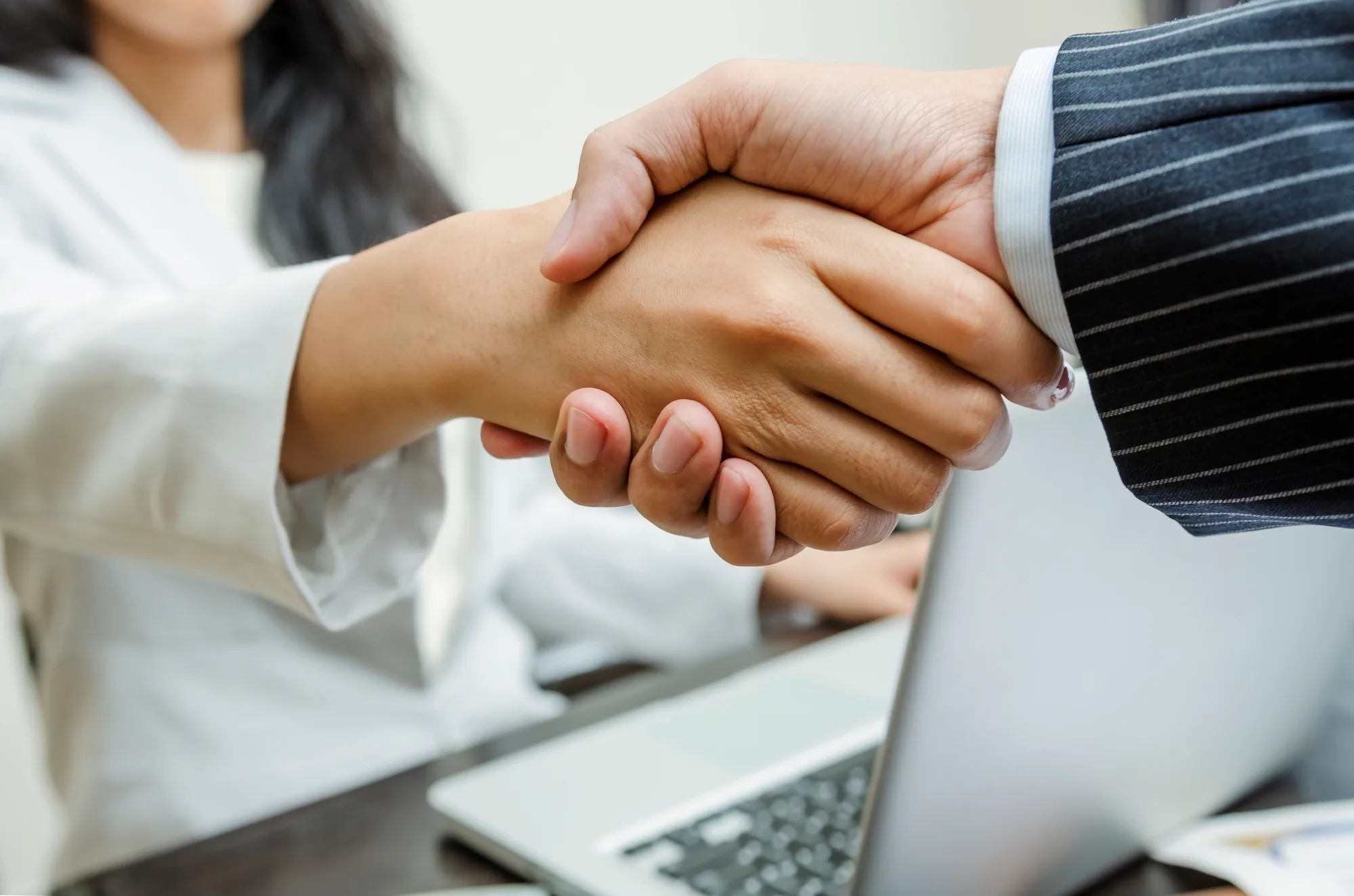 Close-up of a handshake between two professionals at a laptop
